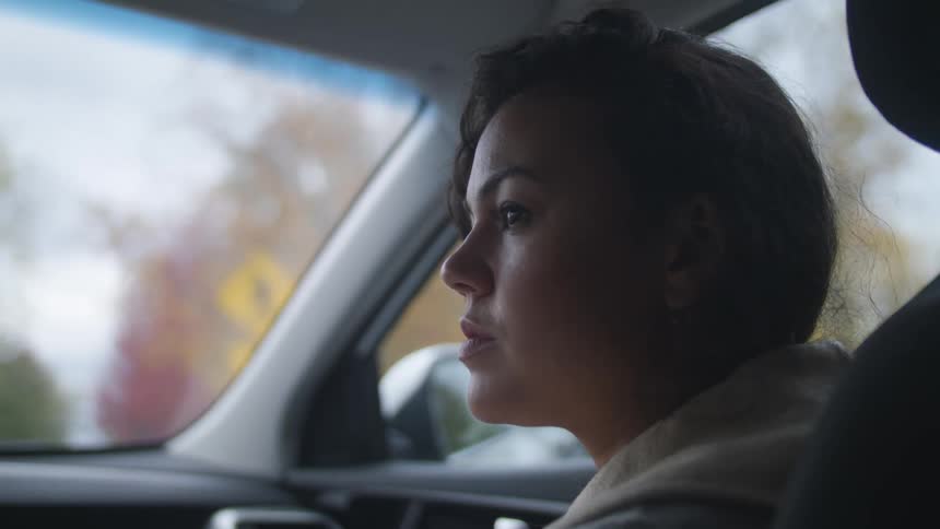 A woman is driving a car smiling and trees can be seen from the window