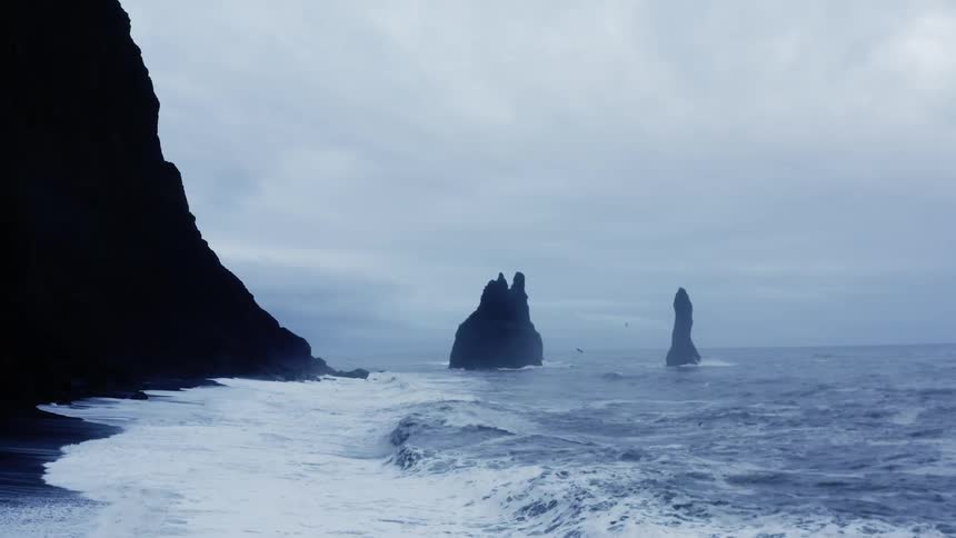 Sea waves wash onto the shore of a tall cliff