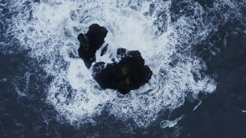 Aerial view of ocean waves crashing on a rock promontory