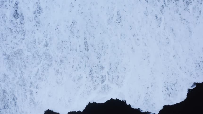 Foamy waves break against black sand beach