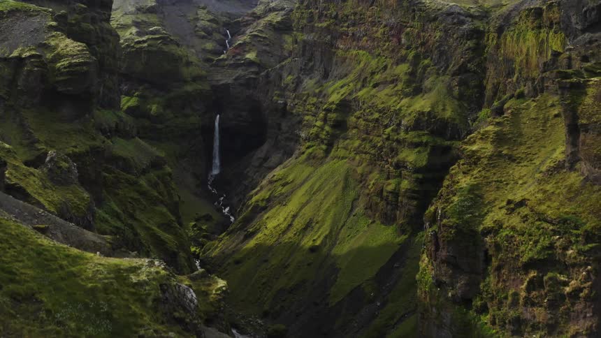 Aerial view of waterfall cascading down mountainside from a great height seen from valley