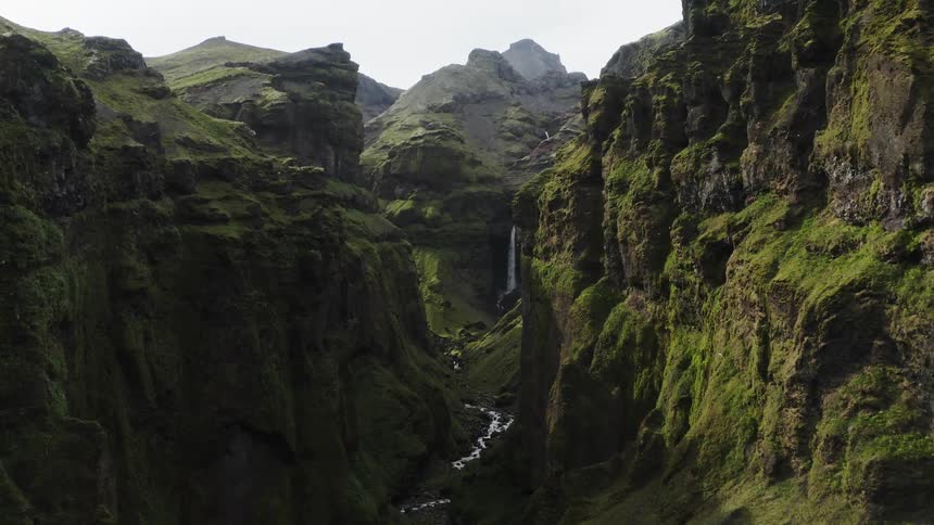 A canyon with a river and a waterfall with the sky and clouds in the background