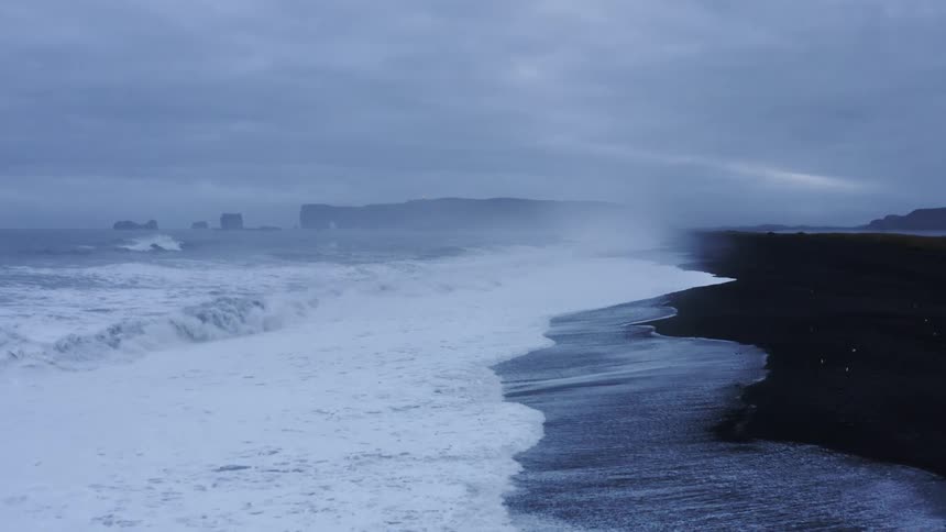 Waves roll onto a beach under a cloudy sky