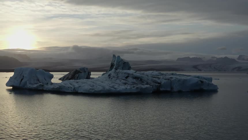 An iceberg with snow and ice surrounded by water with the sky and clouds in the background