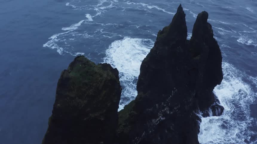 Aerial view of ocean waves crashing on a dark rock promontory