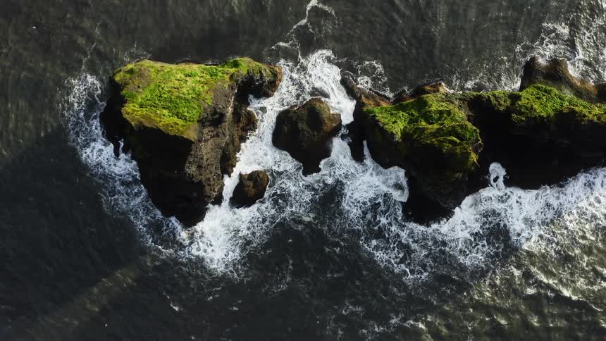 Top down aerial view of ocean waves crashing on rock promontories on the sea