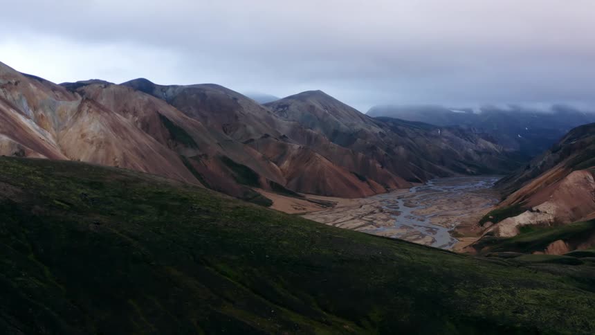 Aerial view of a river flowing on a valley between mountains under the clouds