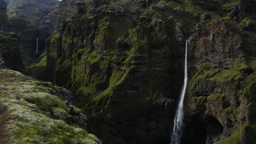 Aerial view of a person standing on the edge of a gorge in front of a waterfall