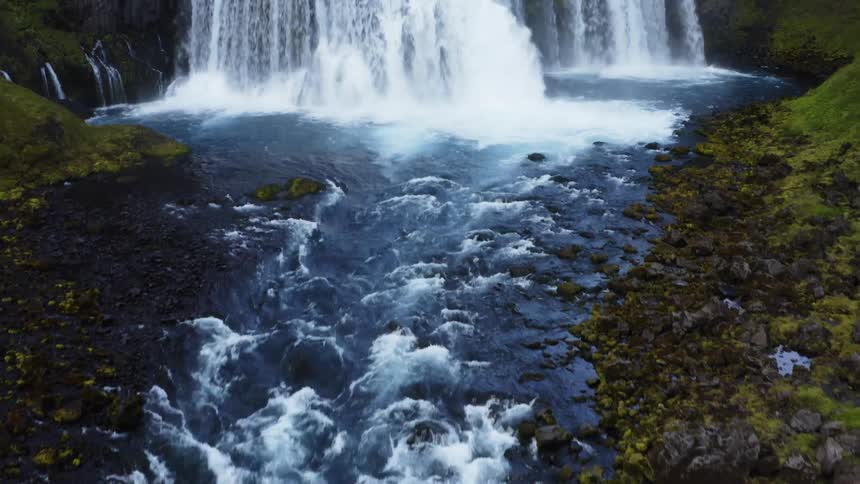 Waterfall flows between mountains and into pool leading to rapids