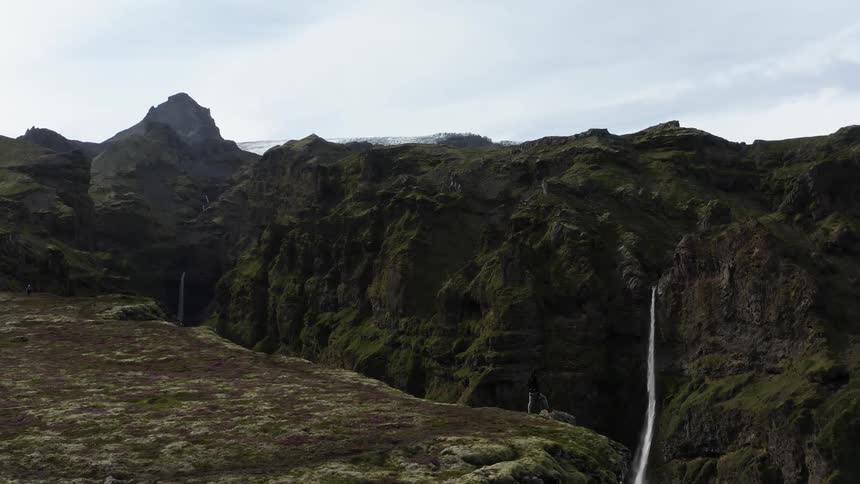 Waterfall flowing from a mountain range with peaks high in a cloudy sky