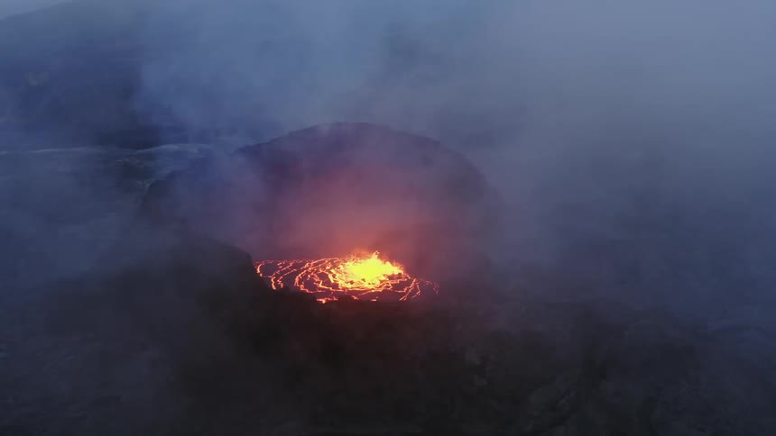 Aerial view of active volcano with a large opening at the top through which gases and lava are forced out