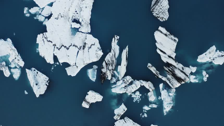 Bird flies across ocean between ice and ice covered islets as blue ocean reflects ice