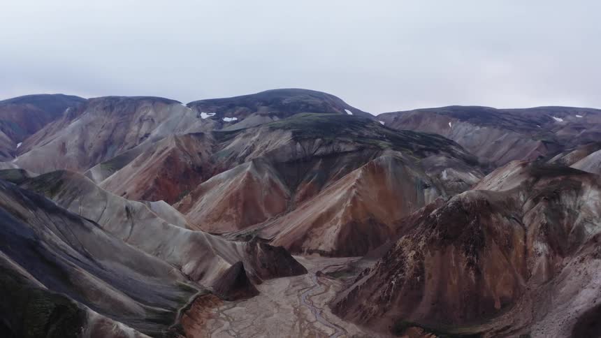 River flows through wider riverbed between mountains under overcast sky