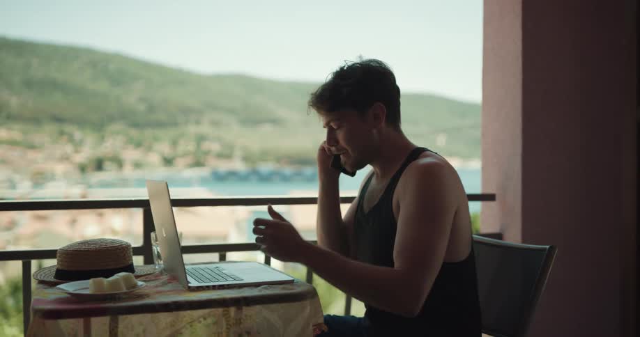 A man sits at a balcony table talking on a cell phone sternly