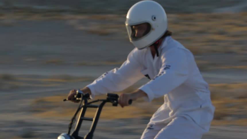 The sun reflects off a helmet visor as a man rides a motorbike on a dirt trail