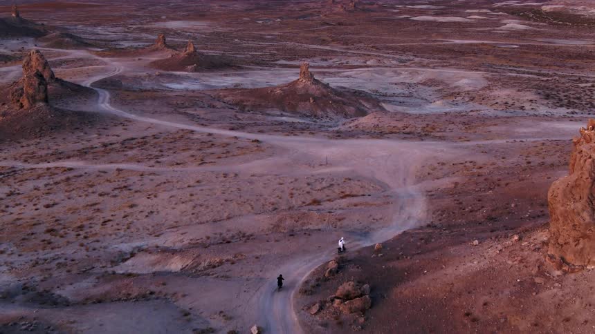 Two people riding motorcycles on a dirt road in a desert landscape