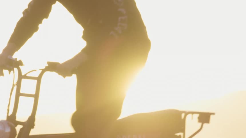 Young man wearing a black suit and crash helmet driving a motorcycle on the desert at sunset
