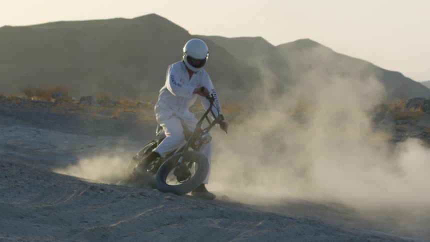 A motorcyclist makes a turn on a dirt bike in arid soil in a desert during the day