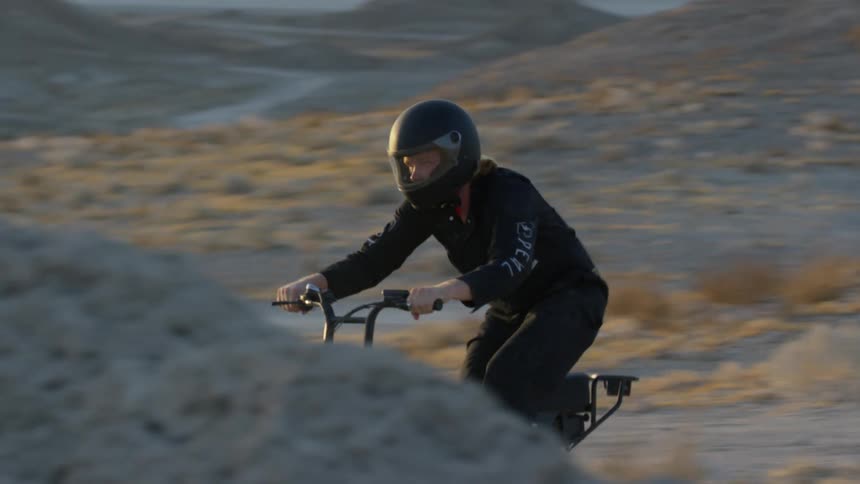 A bicyclist stands up as he does a trick while riding through the desert