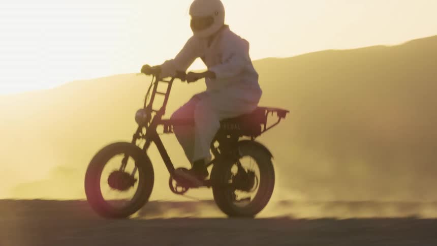 A person with a helmet riding a motorcycle in a desert with the sky and clouds in the background