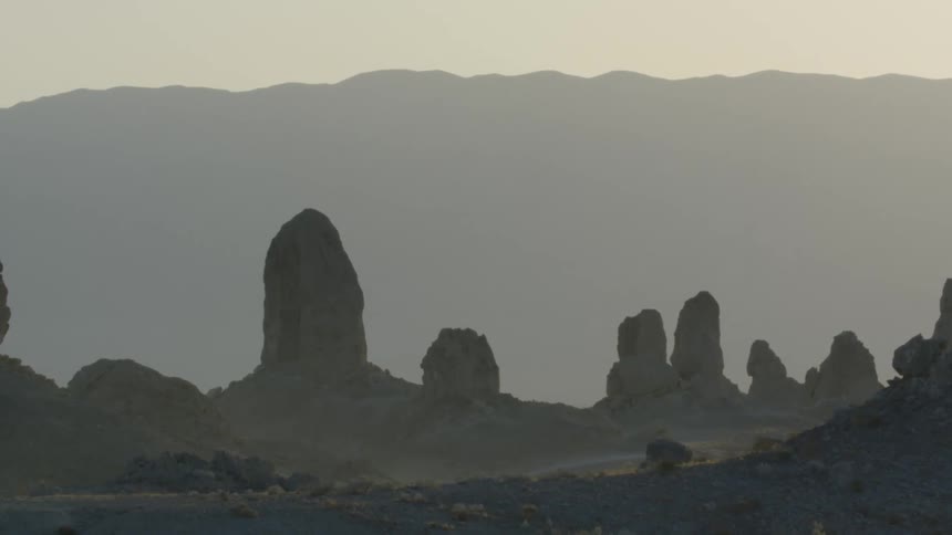 A bird is flying behind tall crags in a rocky wilderness on a hazy evening