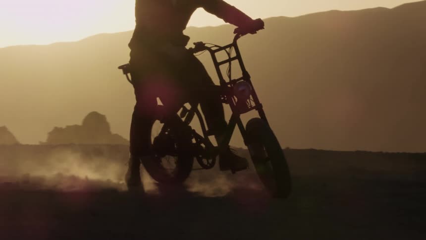 The silhouette of a rider kicking up dust as he makes a turn on a motorbike