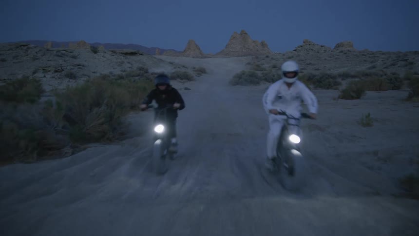 Two people race in the desert on dirt bikes