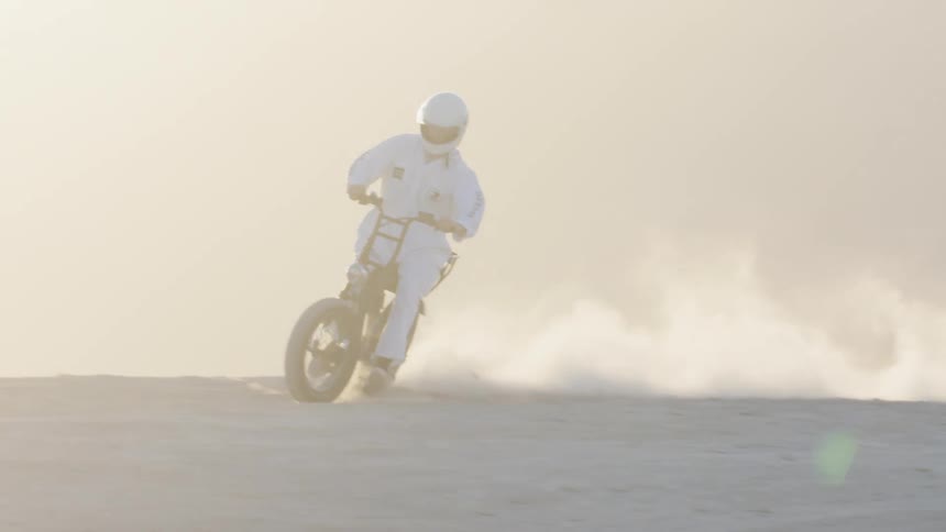 A motorcyclist rides a dirt bike through the arid soil of a desert during the day