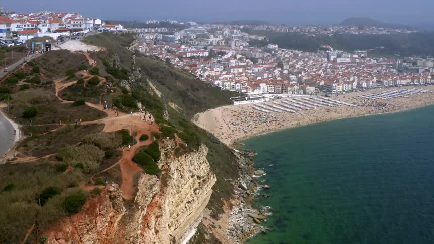 A cliff with people near the coast with buildings the sky and clouds in the background