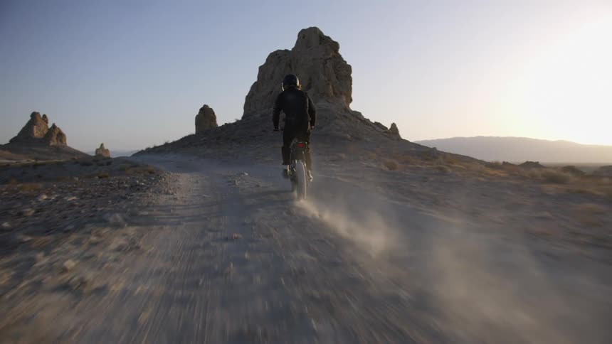 A person is riding an electronic bike on a dirt path in the rocky wilderness at sunset