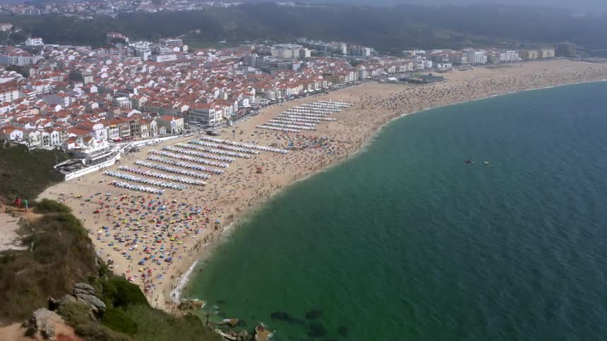 A long wide sandy beach with people wading and sunbathing