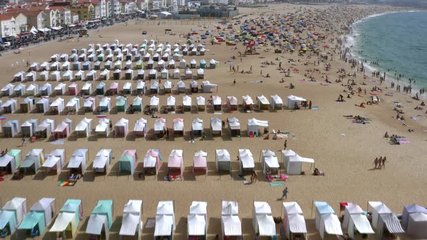 A beach with people tents and umbrellas with buildings in the background