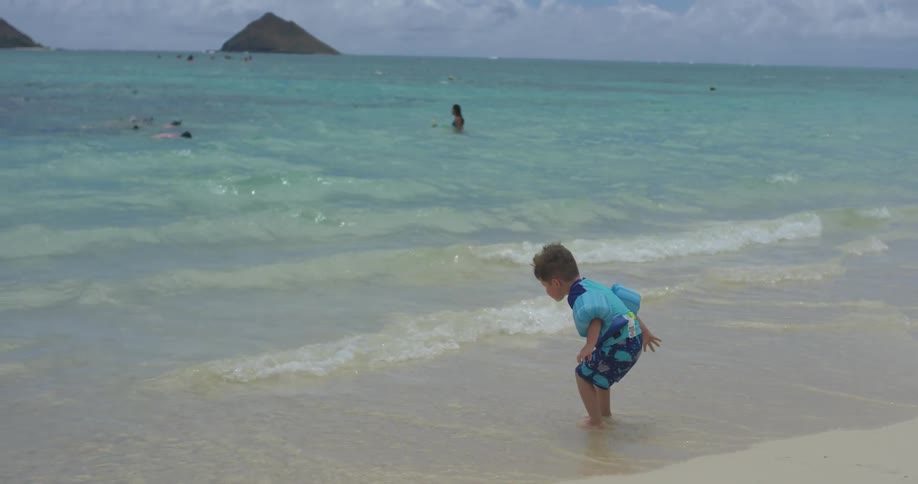 A boy in floaties walks into the water