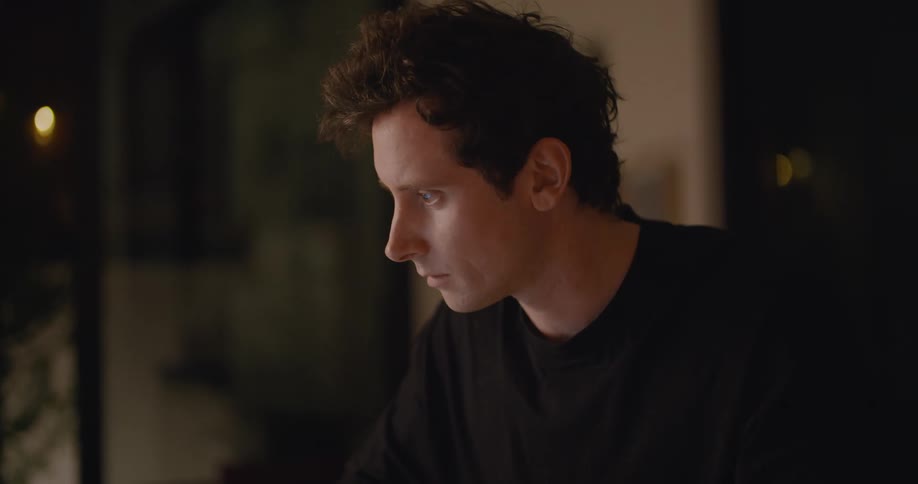 Man in black sweater works on laptop and writes down in notebook