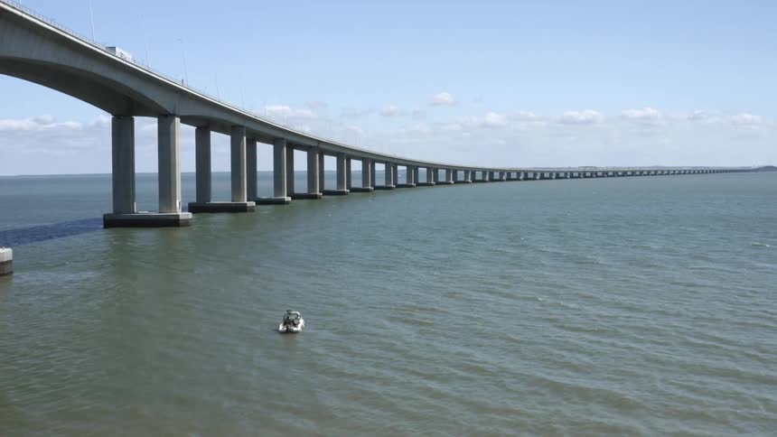 A man sails a boat in the ocean below a bridge