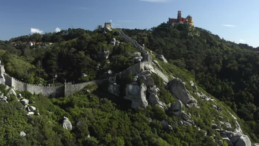 Castles on top of rock covered mountains with a stone wall along the mountainside