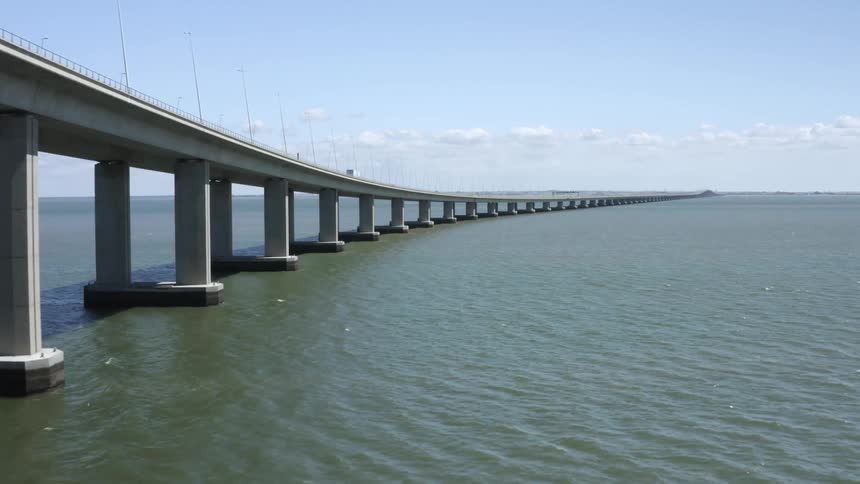 Aerial view of a white van driving over a bridge in the ocean