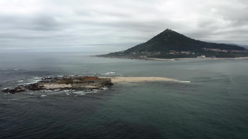 An aerial view of an island in the ocean with a hill on the shore
