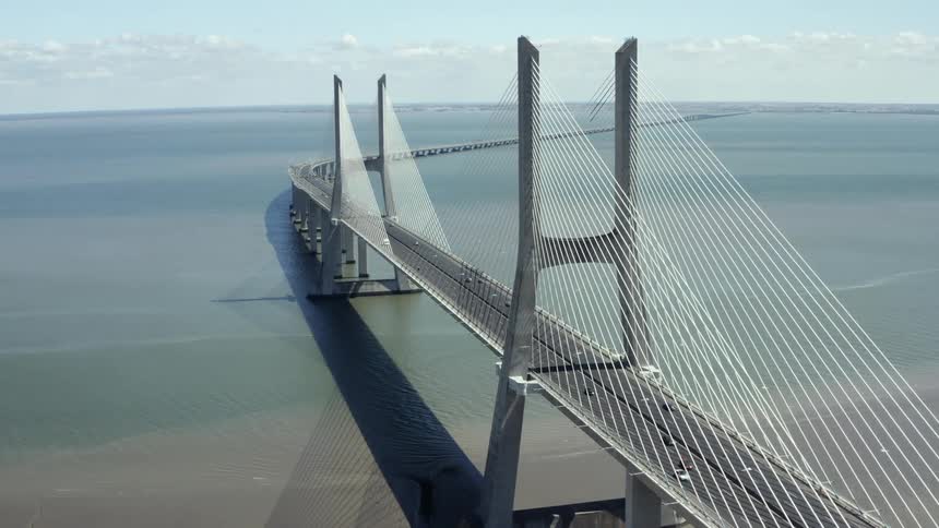 A bridge over a river with vehicles with the sky and clouds in the background
