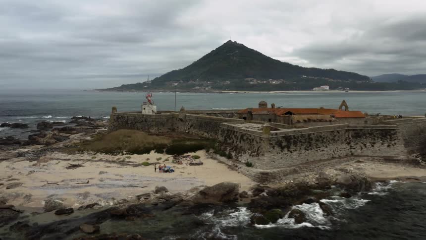 Aerial view of tourists exploring a small island with a lighthouse near a coastline on a dreary day