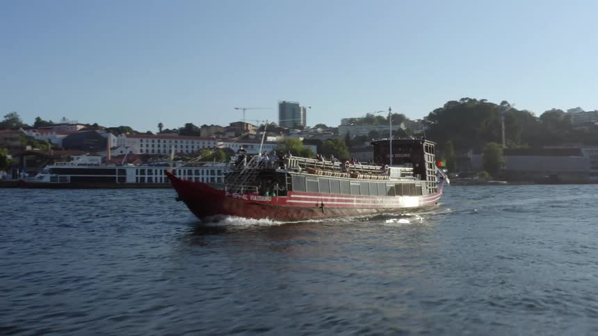 A large boat travels along a river through a metropolis during the day
