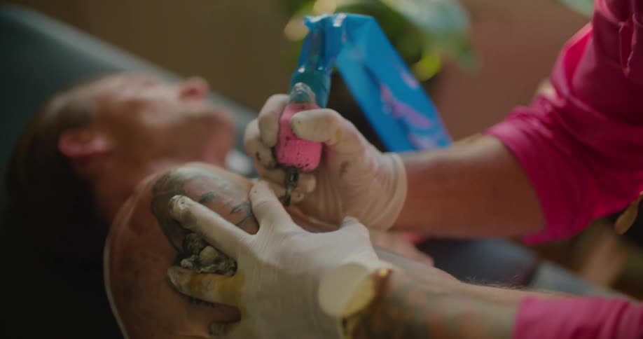 A tattoo artist wipes a mans arm before tattooing