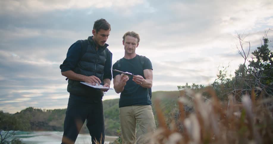 Two men are outside taking measurements on one man is writing on a clipboard