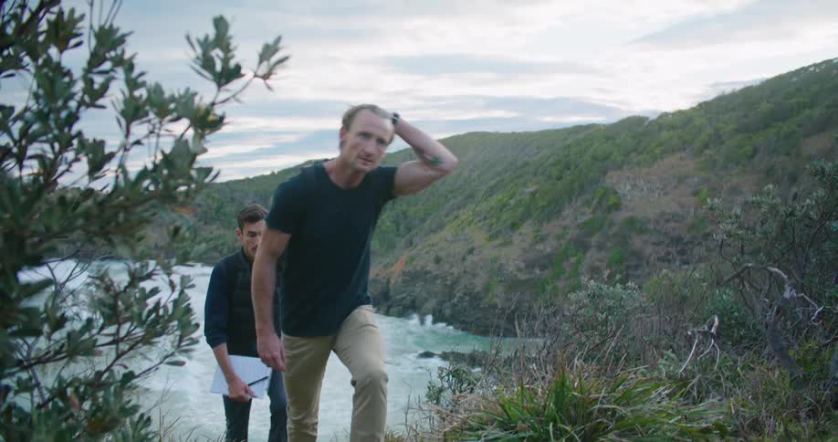 Two men are walking up a hill with a beach behind them