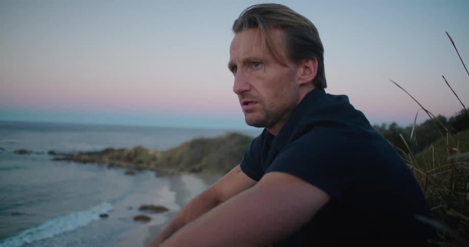 A man sitting at the beach at sunset