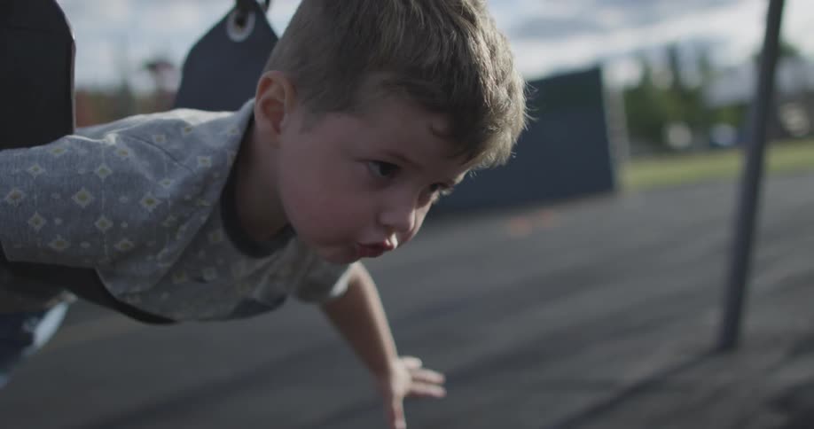 A boy is using a swing in a park with his arms out