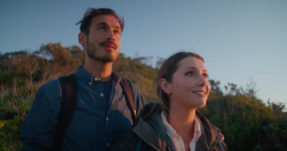 A female hiker raises her smartphone to take a photograph while a male hiker standing behind her points at something in the distance