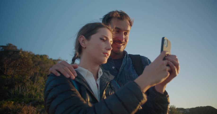 A man and woman are outdoors recording a video on cell phone on a windy day