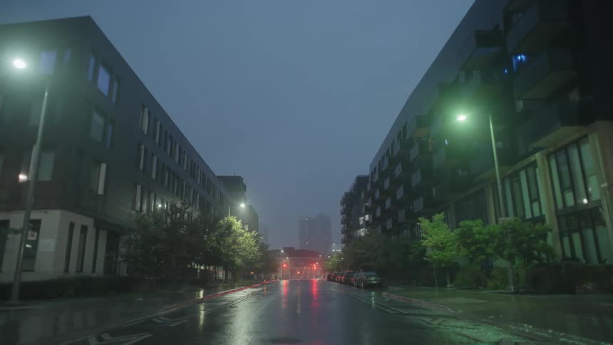 A city street with buildings vehicles and trees with the sky and clouds in the background