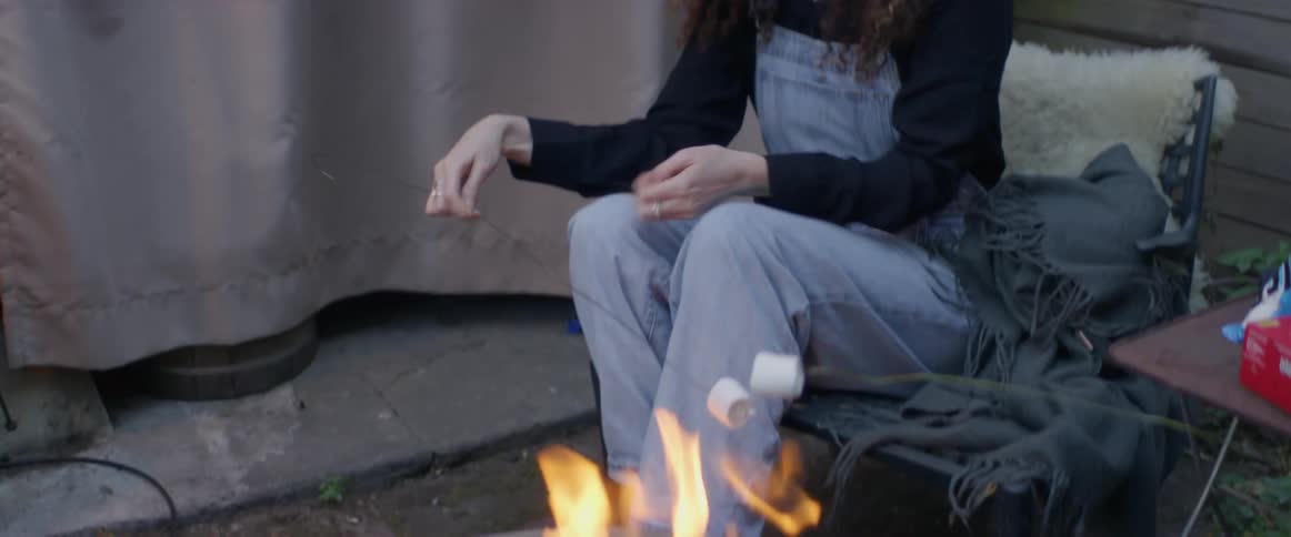 Two women are outside roasting marshmallows over a fire